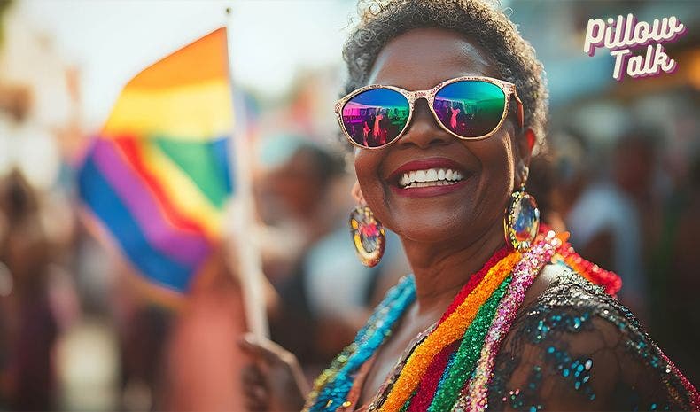 Black man with natural black hair holding a rainbow flag over their head, wearing large white sunglasses, a nose ring, and smiling. A white frame surrounds image, text in magenta “LGBTQ+ Glossary.” "Pillow Talk" in magenta cursive is in upper right corner