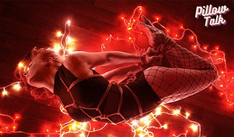Sexy girl on the floor in a black bodysuit, tied up in rope and Christmas lights