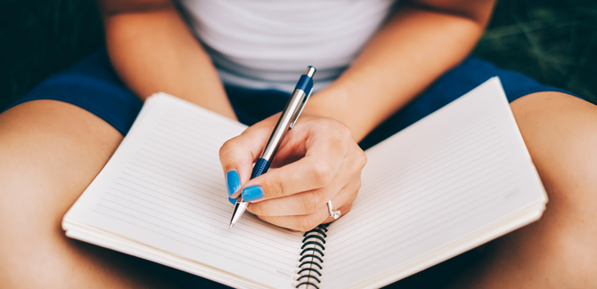 Journal open on the lap of a white woman with blue nail polish and an engagement ring.