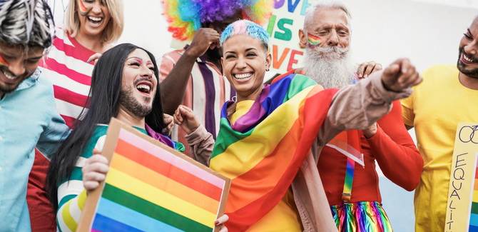 Diverse group of individuals celebrating at Pride with rainbow hair, flags, beads, and signs.