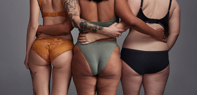 Three people (left to right are mixed raced, black, and white) are standing together with arms wrapped around each other's waists, wearing colored under garments. The camera is focused on their butts, showing curves, cellulite, and blemishes.